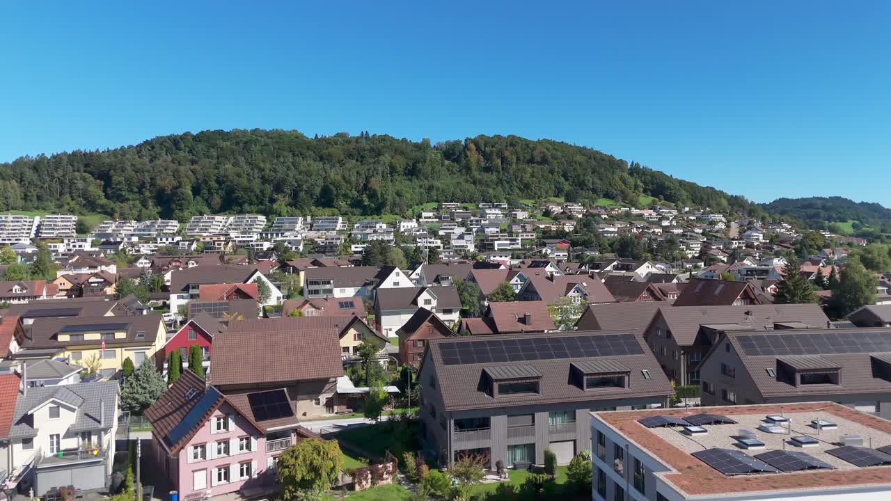 Modern Swiss neighborhood with rooftop solar and efficient housing on a hillside; drone pullback