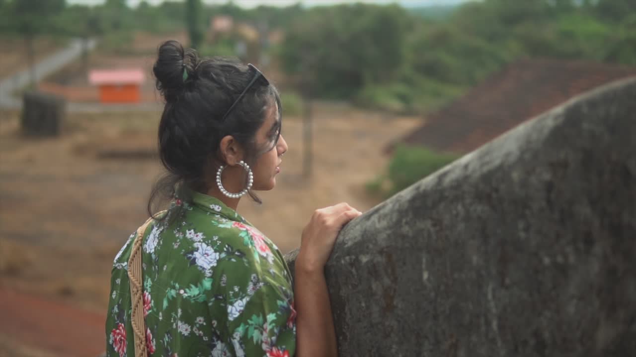 señorita con un vestido verde estampado floral con cabello oscuro mirando una granja en india