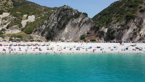 Crowded-touristic-Mediterranean-sand-beach-in-Myrtos,-Greece,-aerial-sideways