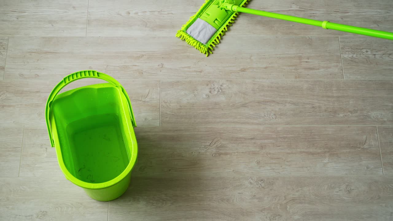 Cleaning the house. Green bucket and mop on the parquet floor. Microfiber brush is mopping the floor. Householding tools. Top view.