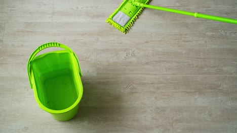 cleaning the house. green bucket and mop on the parquet floor. microfiber brush is mopping the floor. householding tools. top view.