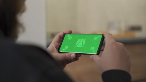 Holding smartphone with horizontal green screen chroma. Mockup. Home lifestyle.