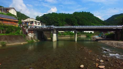 Drone's-perspective-reveals-charming-Japanese-village,-approaching-bridge-over-tranquil-river