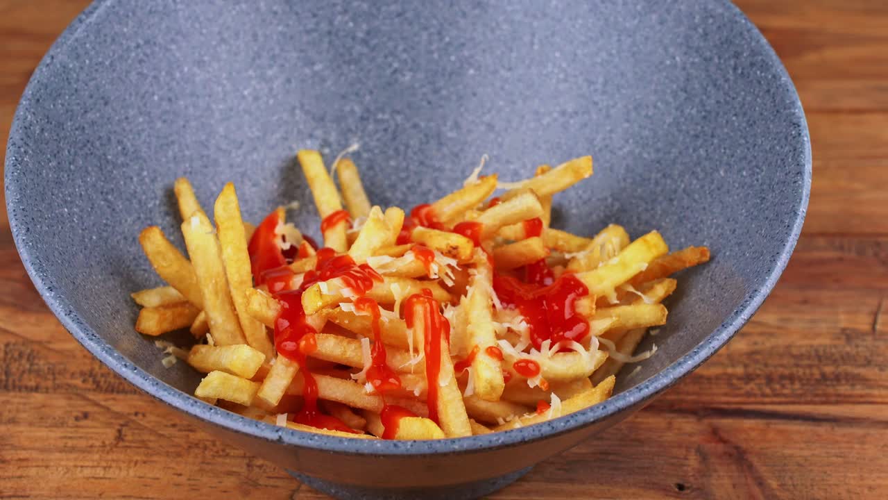 Close up of French fries with grated cheese being bathed in ketchup