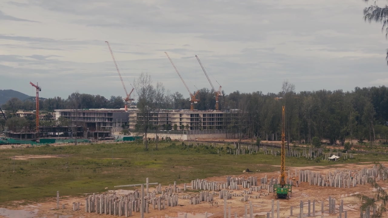 Active construction site featuring concrete foundation poles, tower cranes and apartment complexes under development, showcasing urban growth and residential expansion.