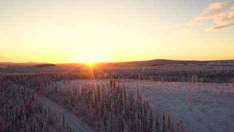 aerial view of sunset over snowy frozen road in deep forest with hills and mountains