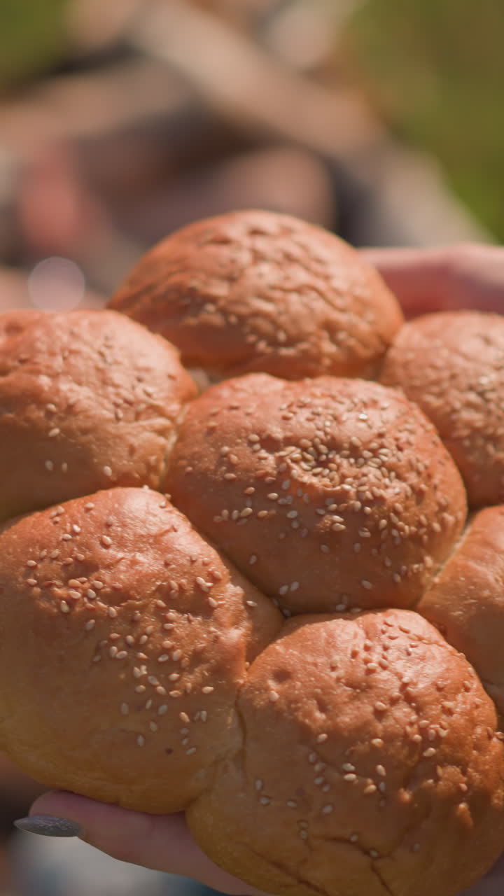 파란색 드레스를 입은 여성의 손이 새로 구운 세 씨  롤을 들고 있는 클러스터의 클로즈업. 배경에는 흐릿한 아이들이 있습니다. 에 초점을 맞추고 있습니다.