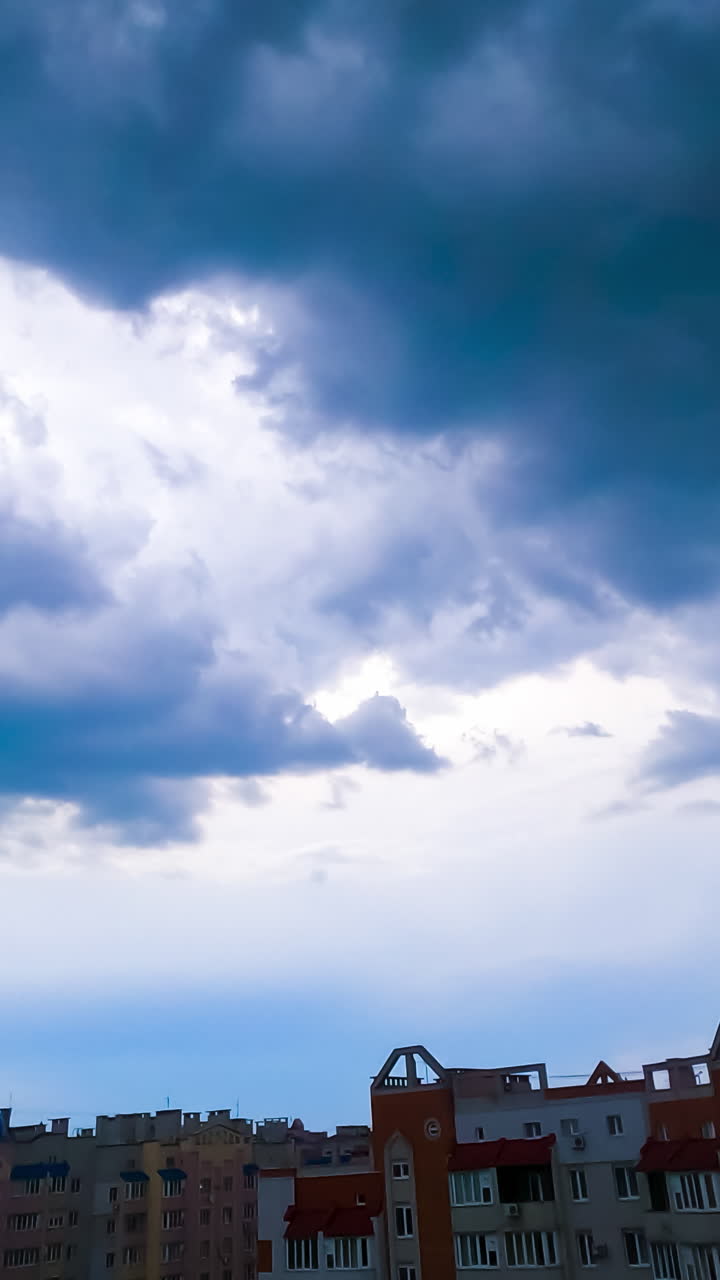 Blue clouds move over the houses in residential area. Timelapse. Yellow splashes appearing in the sky. Vertical video