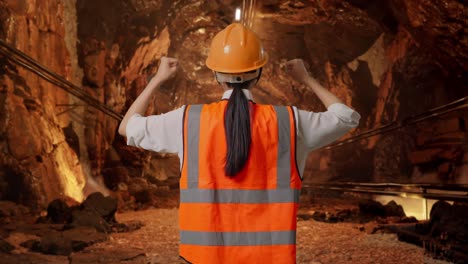 back view of a female engineer with safety helmet raising her hands celebrating while working in underground mine tunnel