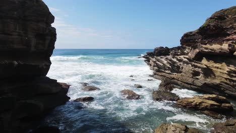 Looking-out-from-a-hidden-rocky-cove-with-waves-crashing-against-a-coastal-headland