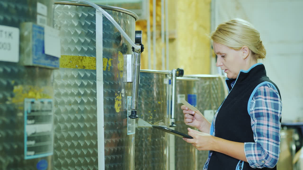 женщина с планшетом работает возле бака с продуктами проверяет бирку на бочке контроль качества в пищевой промышленности