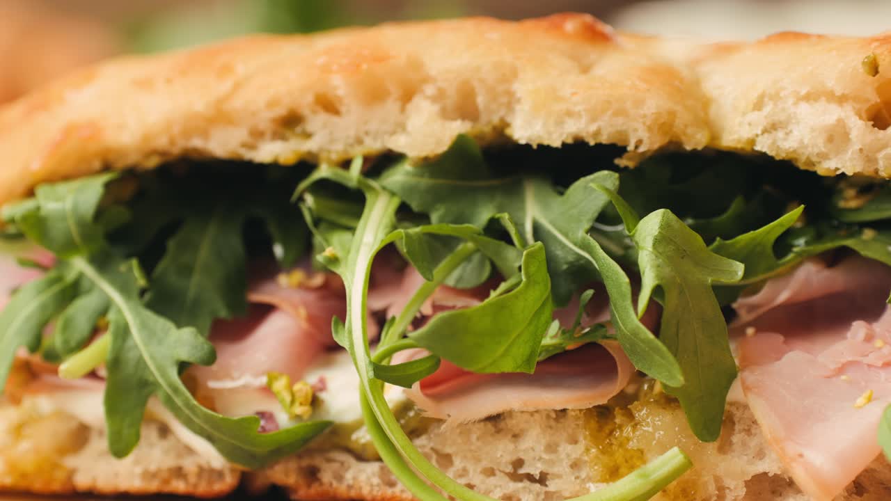 Mortadella ham sandwich, Traditional italian focaccia filled with thin pesto slices of mortadella, served by chef man in cafe restaurant. Macro of traditional italian spanish tapas antipasti.