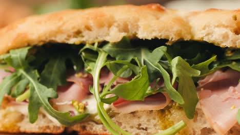 mortadella ham sandwich, traditional italian focaccia filled with thin pesto slices of mortadella, served by chef man in cafe restaurant. macro of traditional italian spanish tapas antipasti.