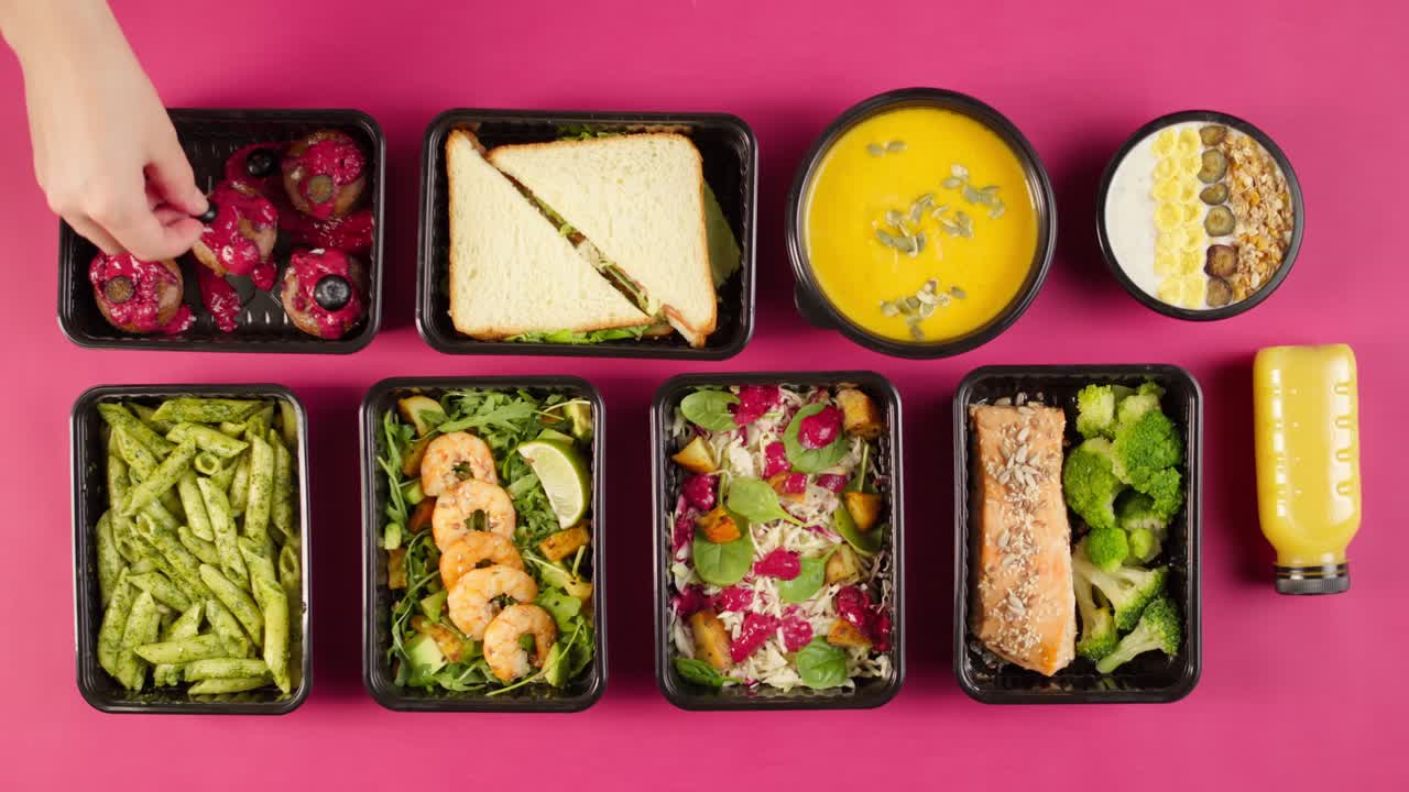 Contenedores de comida saludable con platos variados sobre fondo rosa.
