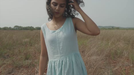 shot of a woman in a blue dress combing her hair with her hand in a wide field