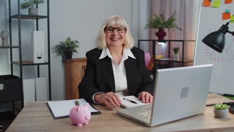 Senior-business-woman-waves-hand-palm-in-hi-gesture-greeting-welcomes-someone-webinar-at-home-office