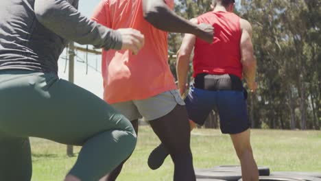 grupo de ajuste diverso corriendo a través de neumáticos en una carrera de obstáculos en el sol