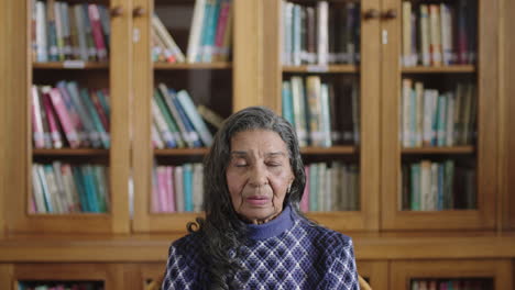 Porträt-Einer-älteren-Indischen-Frau-In-Der-Bibliothek,-Entspannt-Und-Erleichtert,-Wenn-Sie-In-Die-Kamera-Blickt