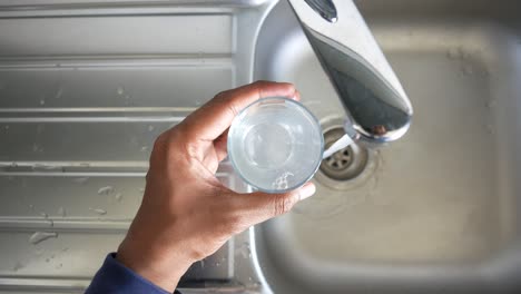 persona llenando un vaso con agua de un grifo de la cocina