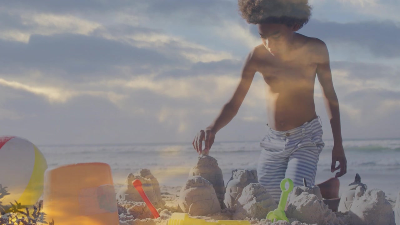 Menino alcançando a areia e moldando castelos de areia na praia para lazer, com nuvens sonhadoras sobrepondo a cena.