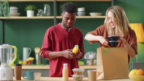 una joven pareja multiétnica descargando alimentos saludables de una bolsa de papel