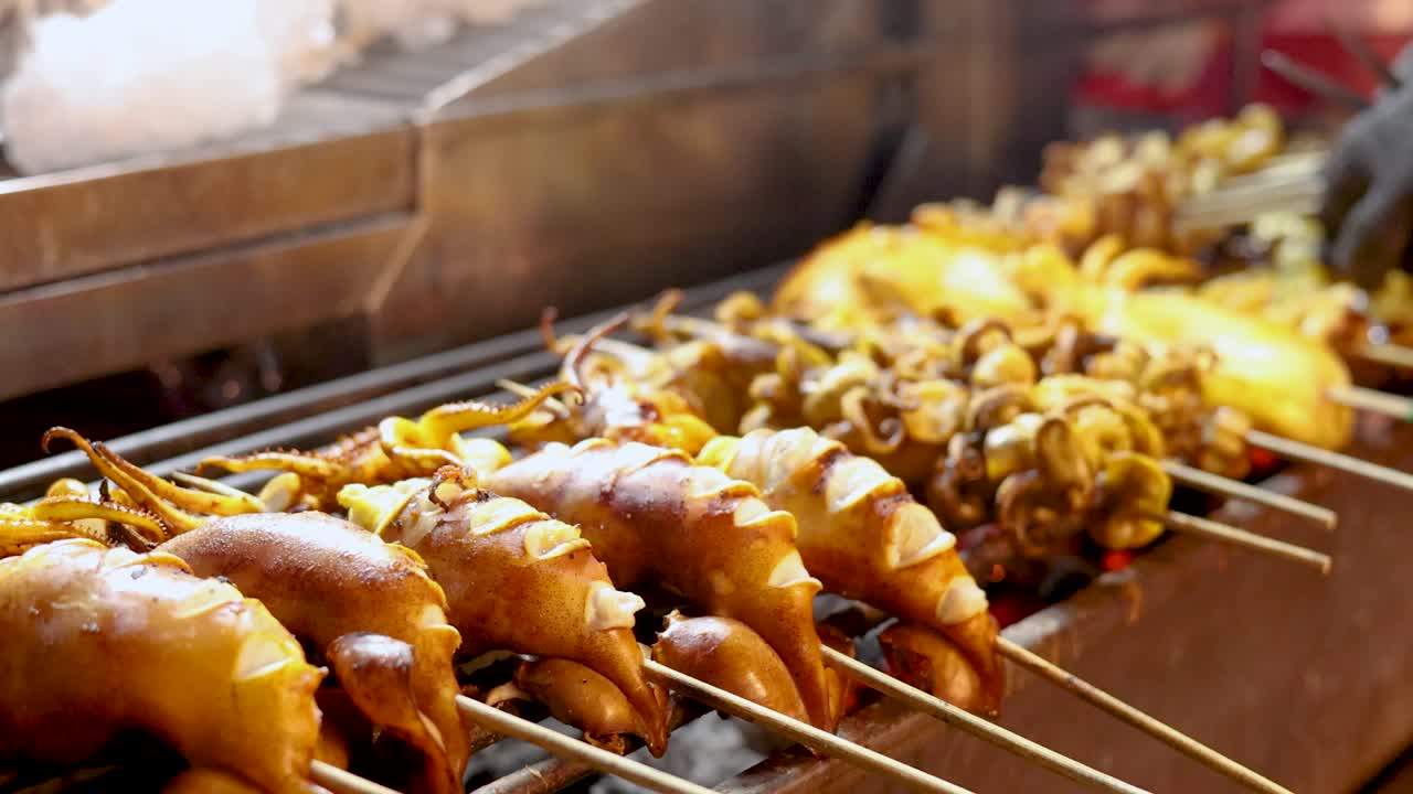 Close-up of squid skewers grilling over open flame, vibrant lighting, slight camera movement, bustling atmosphere