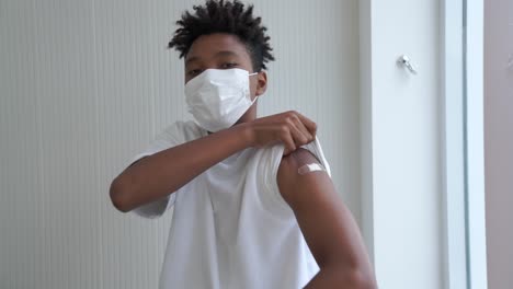 african american teenager showing covid-19 vaccine bandage merrily