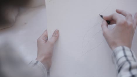 artist delicately using a black pencil to make a trace on paper before drawing