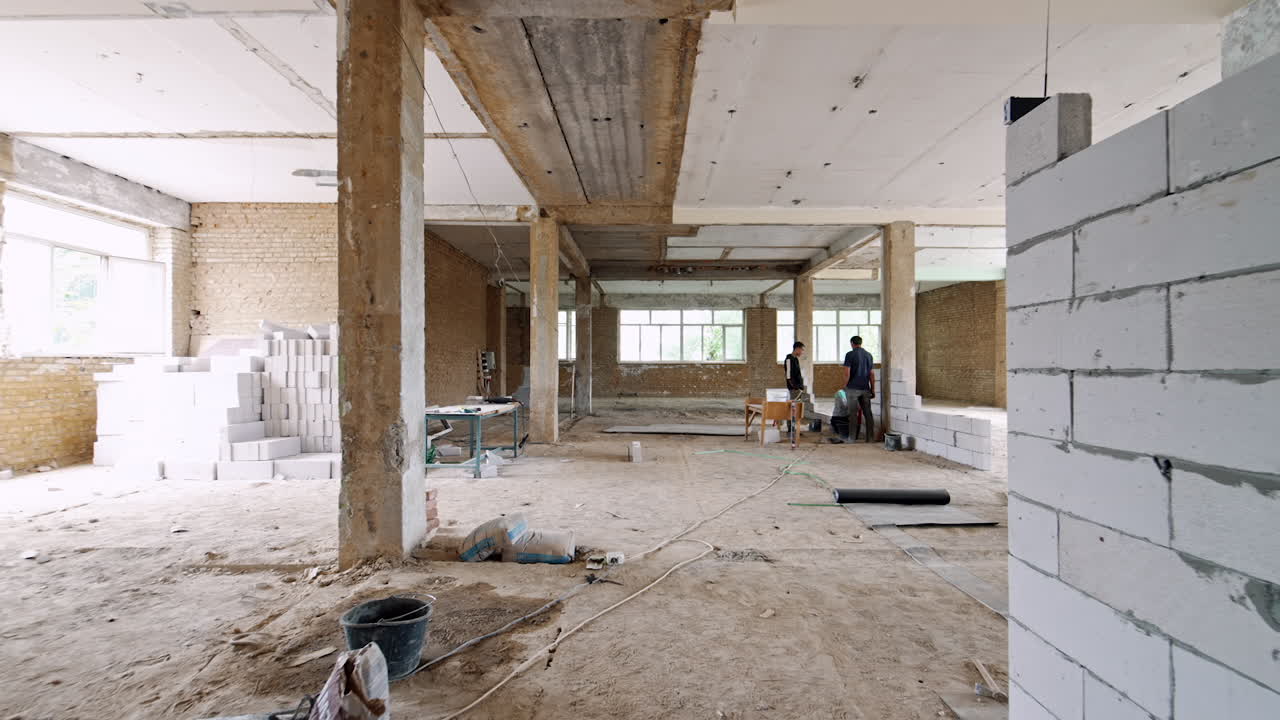 A new wall of white big bricks is built in the premise of an old building. Three builders are working in the room.