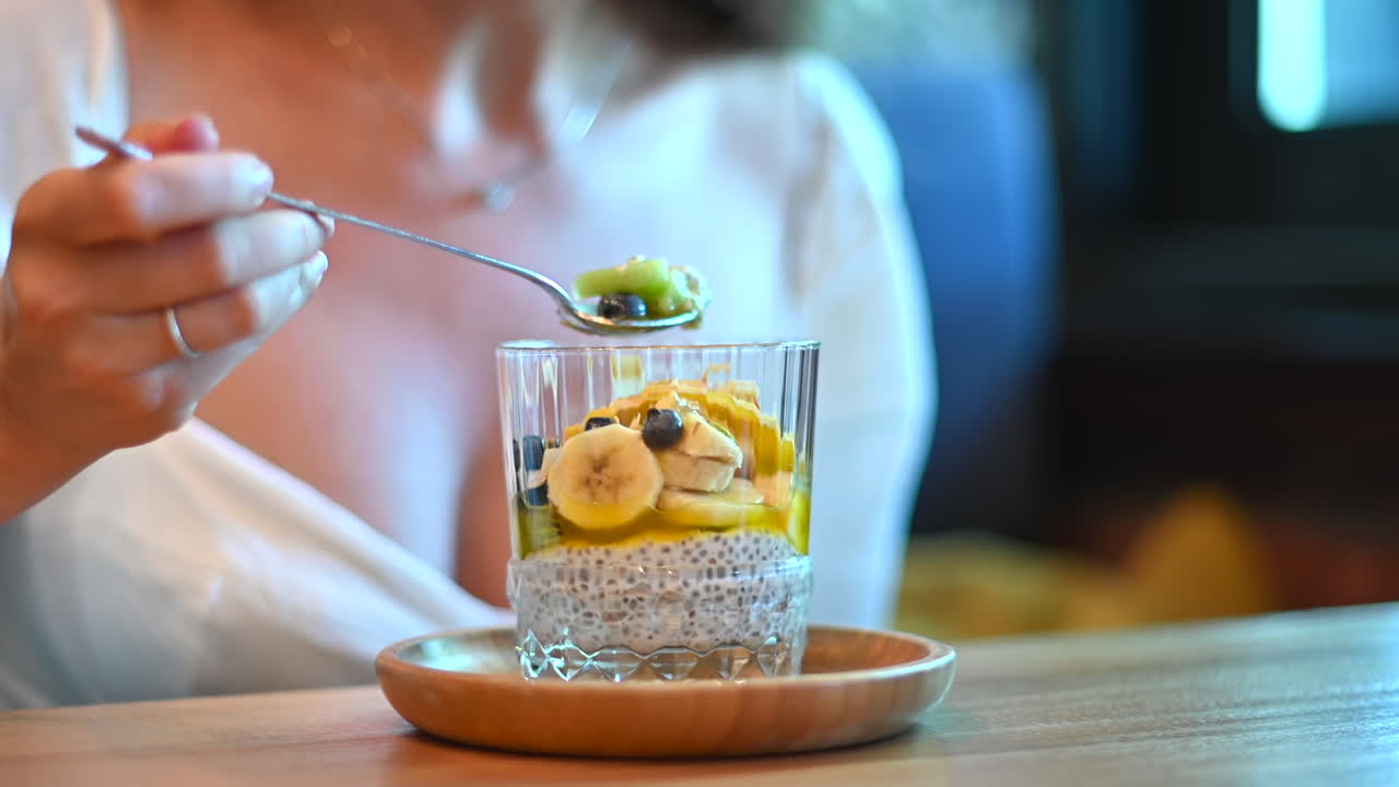 Donna in abito bianco che mangia un budino di chia con frutta al ristorante