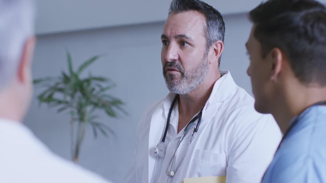 médico caucásico senior discutiendo con diversos colegas en una reunión del personal del hospital