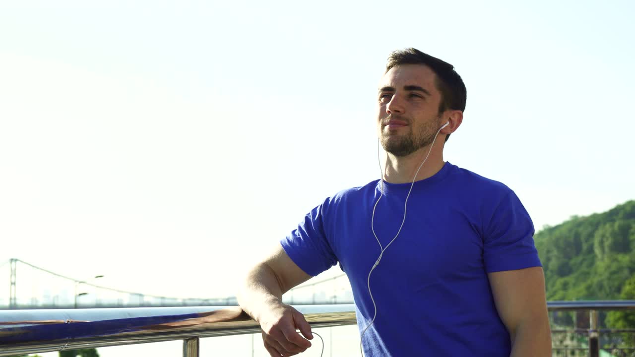 Happy handsome man enjoying listening to music outdoors after working out