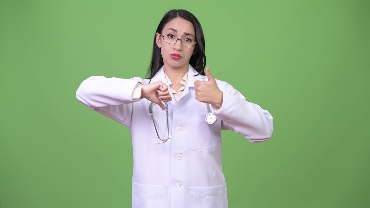 Young beautiful Asian woman doctor choosing between thumbs up and thumbs down