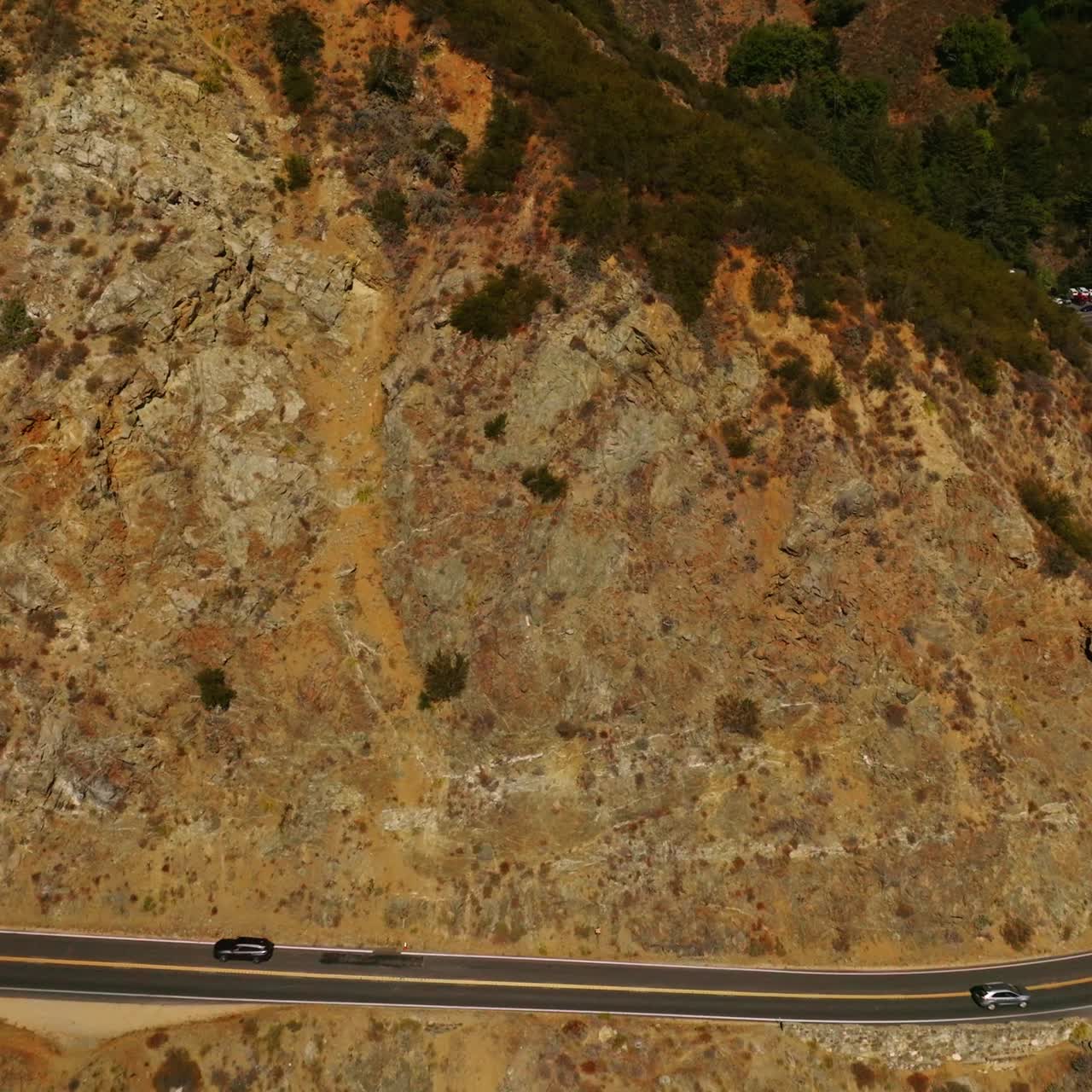 Stunning mountains with little greenery growing on. Road in the middle of rocks at the edge of cliff. Sunny day footage from air