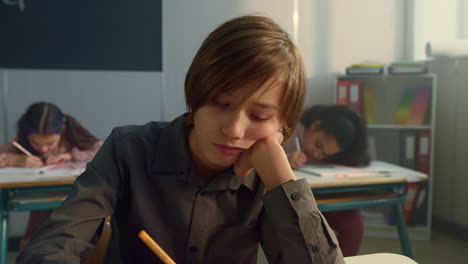 niño cansado sentado en el aula. niño alegre aburrido durante la lección