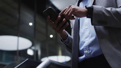 Midsection-of-african-american-businessman-using-smartphone-in-lobby-of-modern-office