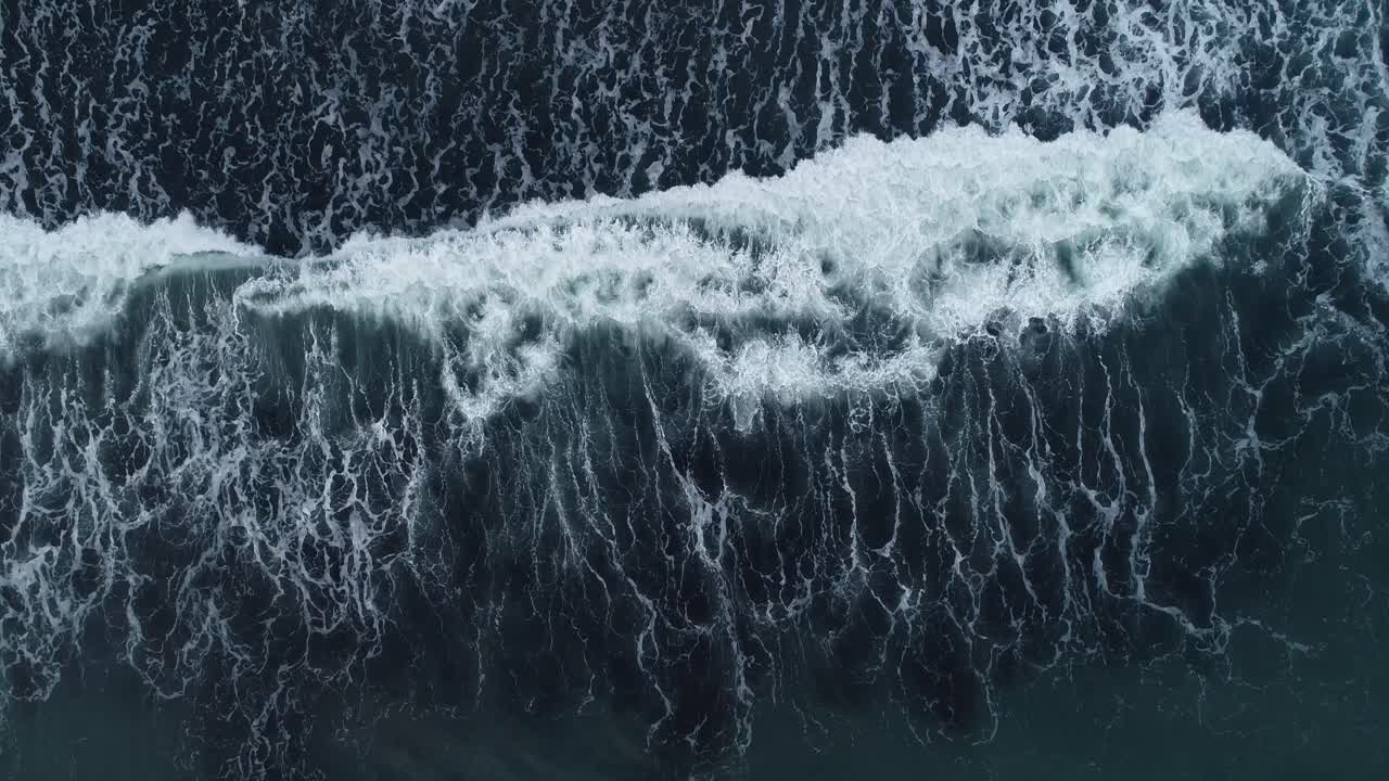 Birds eye drone footage of waves breaking over a black sand beach in Iceland