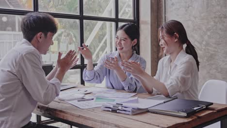 young asians clap each other for a successful project. in smart casual wear and smiling while working in a creative office