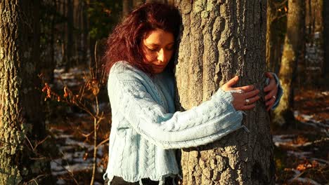 Joven-Pelirroja-Caucásica-Abrazando-Un-árbol-En-El-Bosque-Al-Atardecer,-Tiro-Medio