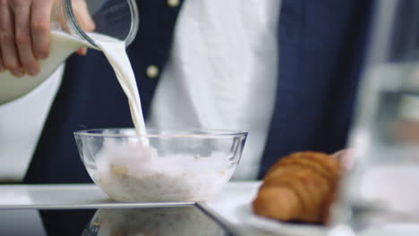 Closeup-man-hand-pouring-milk-into-glass-bowl-with-cornflakes-in-slow-motion.