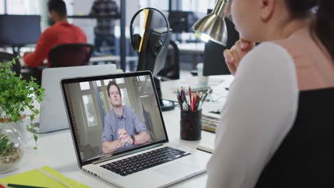 Caucasian-businesswoman-sitting-at-desk-using-laptop-having-video-call-with-male-colleague