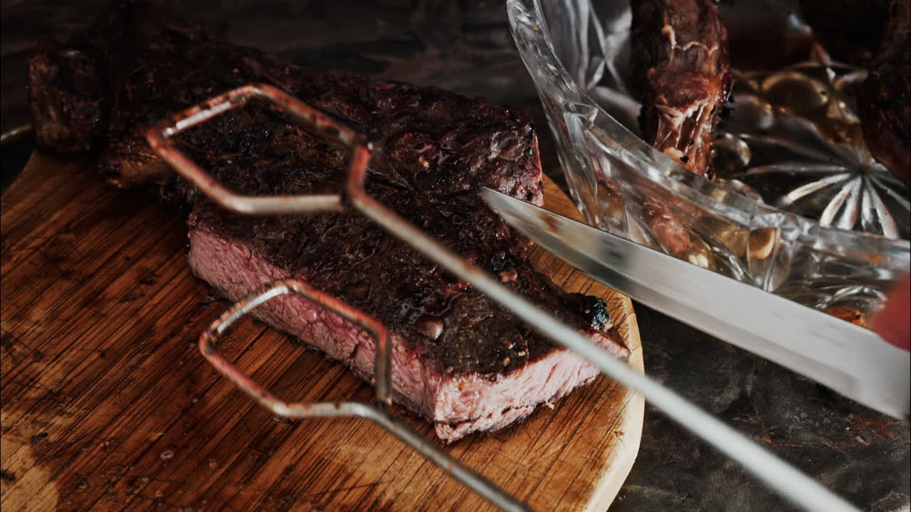 Close-up of a man's hand carving a grilled steak on a rustic wooden cutting board