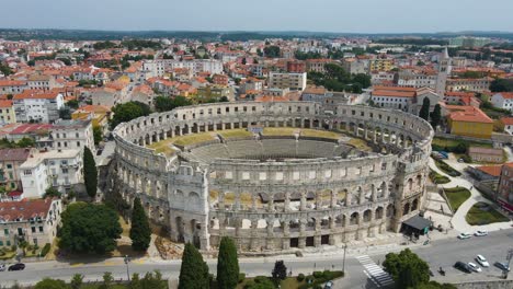 aerial forwarding shot over roman arena in pula, istria, croatia which is a unesco world heritage site on the side of a road on a bright sunny day