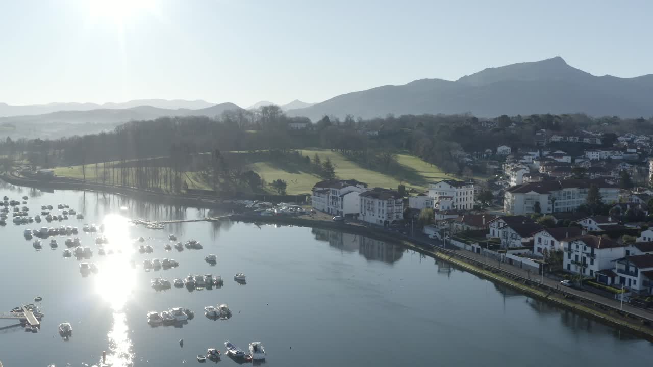 Bright sunny day at Saint-Jean-de-Luzover, Nivelle river, port and moored boats, sun reflects on water, La Rhune mountain in background, Basque Country in France. Aerial drone, copy space