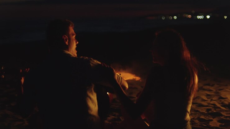 романтическая пара играет на гитаре у костра на пляже ночью