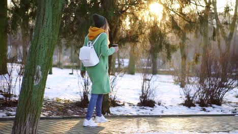 mujer caminando con bebida caliente por el parque de la ciudad de invierno o el bosque en cámara lenta