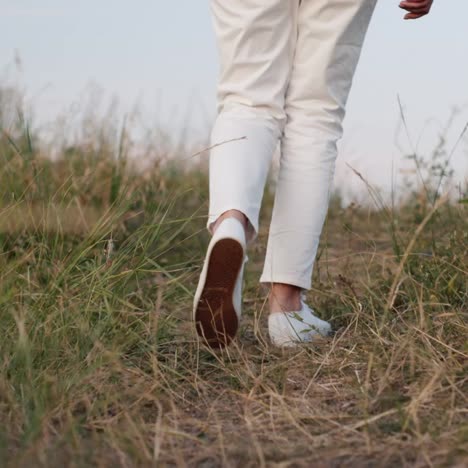 las piernas de una mujer vestida de blanco caminan por el camino entre la hierba