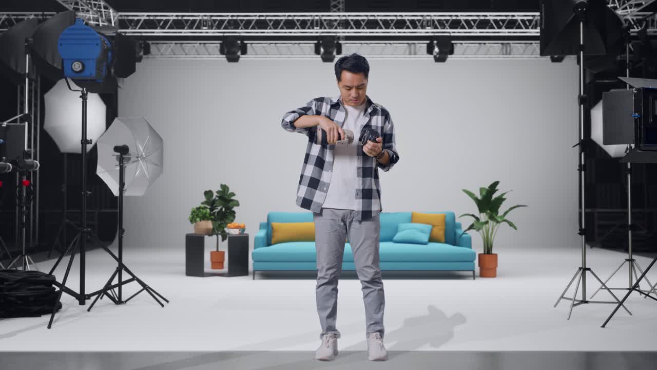 Fotografo asiatico a figura intera che cambia l'obiettivo della fotocamera prima di usarla per scattare foto mentre è in piedi nello studio
