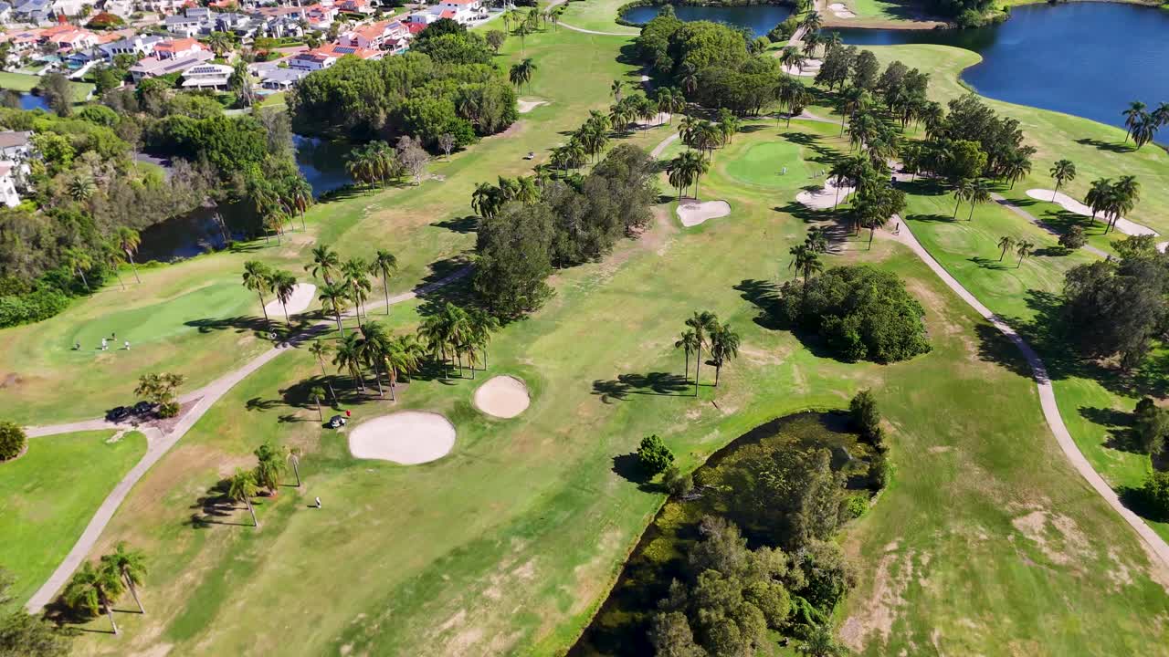 Sunny drone flyover of lush golf fairway with sand bunkers, lakes, trees, and houses