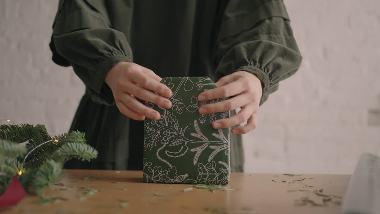 una mujer en una mesa de madera decora un regalo de navidad verde